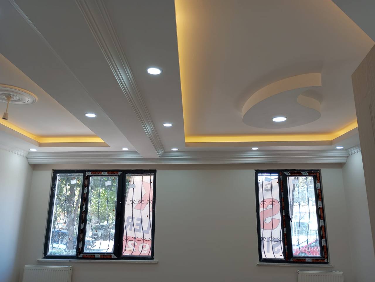 Kavisli alçıpan detayı, sarı ışık bandı ve beyaz spotlar bulunan dekoratif tavan.