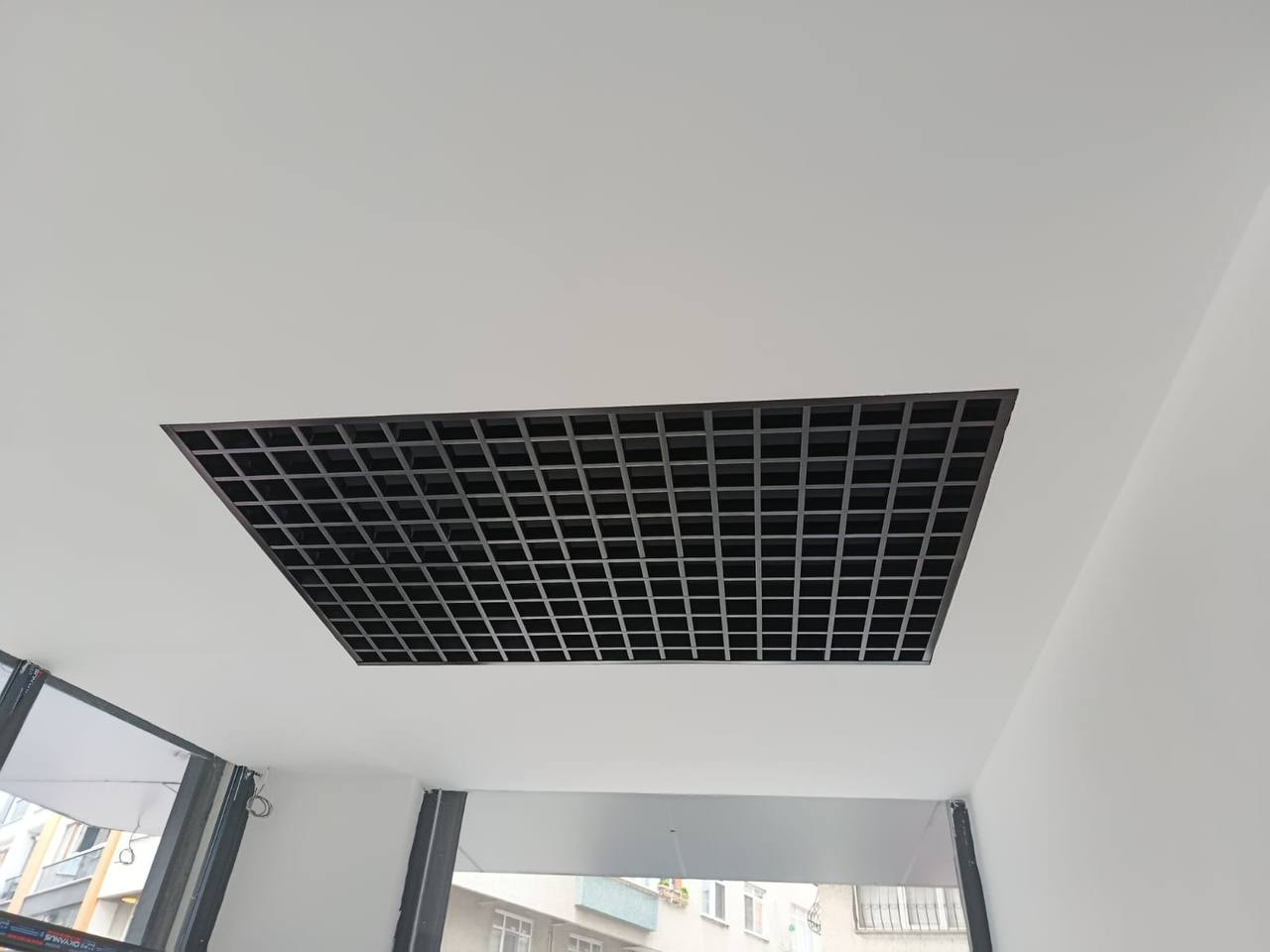 Beyaz tavan içine yerleştirilmiş siyah ızgara biçiminde kare modüllü tavan detayı.